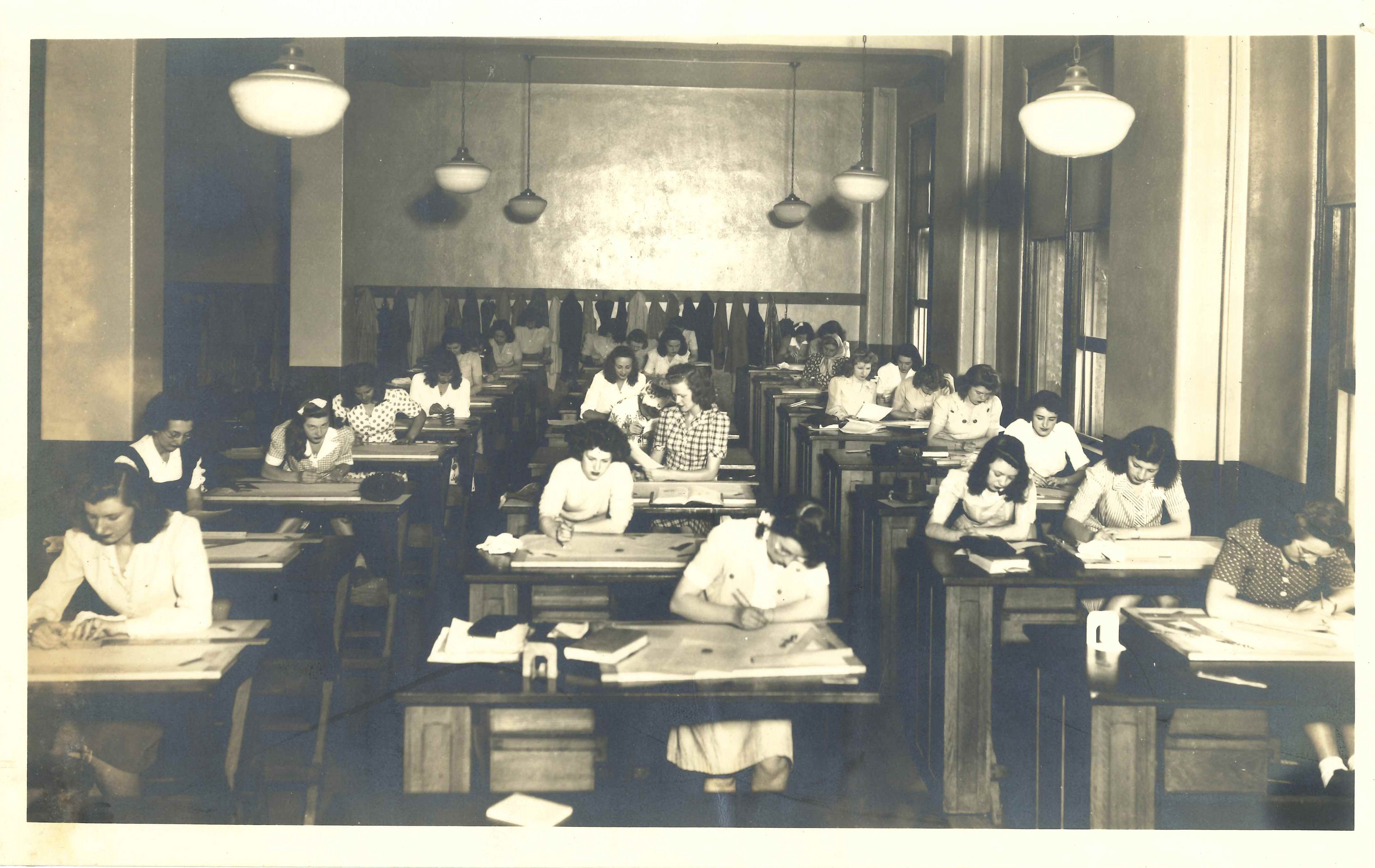 A group of students working at desks inside a long hall. 