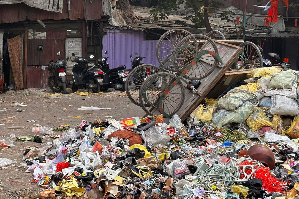 A mound of garbage with a cart turned upside down up top. Four motor bikes are visible in the background.