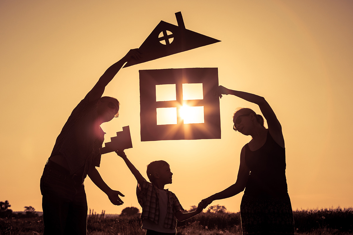 A silhouette of three people, two adults and one child, holding a silhoutted paper cut out of a house.