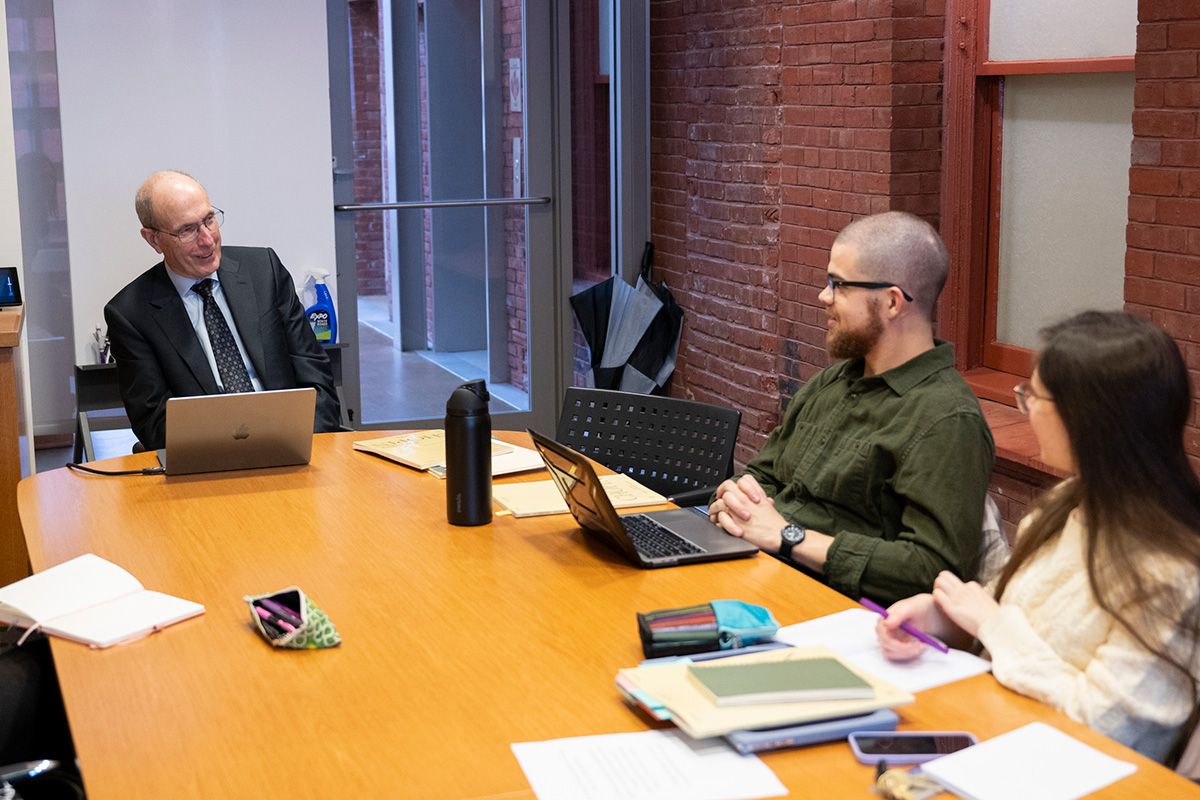 Jeffrey Kallberg sitting at a table with a laptop in front of him. Two other people, also with lapstops in front of them sit around the table, which appears to be in a classroom.