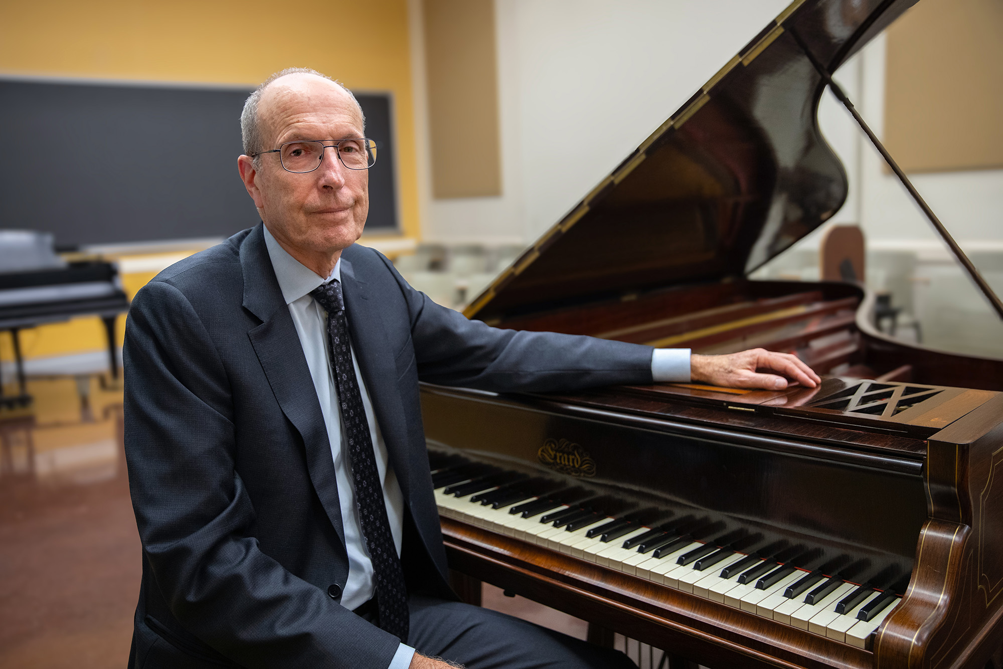 Jeffrey Kallberg sitting at a grand piano, his arm outstretched over top