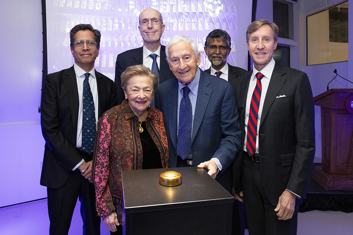 A group of people standing at a podium with a gold button. People include, from left to right, Ramanan Raghavendran, Diana Vagelos, Jeffrey Kallberg, Roy Vagelos, Vijay Kumar, and Larry Jameson.