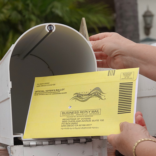 An open mailbox with a yellow envelope that is an "Official Voter's Ballot" being sent to the Registrar of Voters in San Diego, California