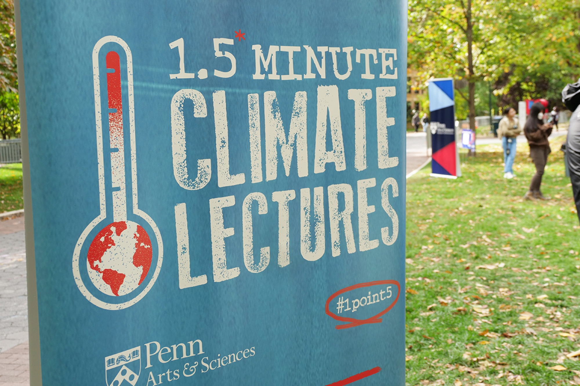 Sign that reads 1.5 Minute Climate Lectures with blurred people and grass in background.