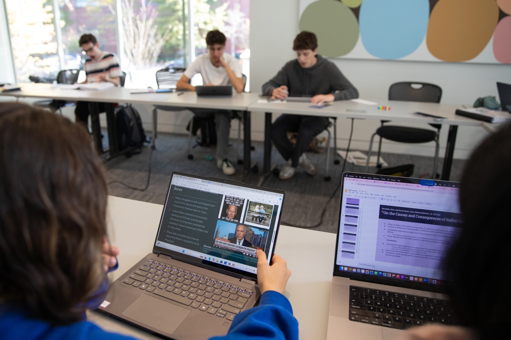 Two computer screens visible, with heads of the people looking at them blurry in the foreground.