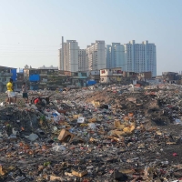 A mound of garbage at the Deonar landfill in Mumbai. A skyline of buildings appears in the background.