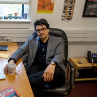 J.C. Cloutier at his desk with a coffee mug and computer in front of him, and other stuff around him.