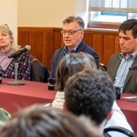 A group of people sitting at a table, as part of a panel conversation. The backs of the audience heads are visible at the bottom of the shot.