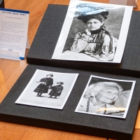 Three old black-and-white photographs laid out on black paper with archival book material open to the right and other images to the left. 