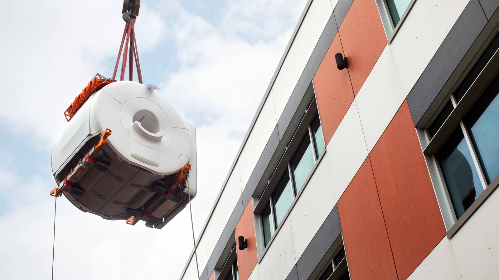 An fMRI machine dangling from a crane outside of a building.