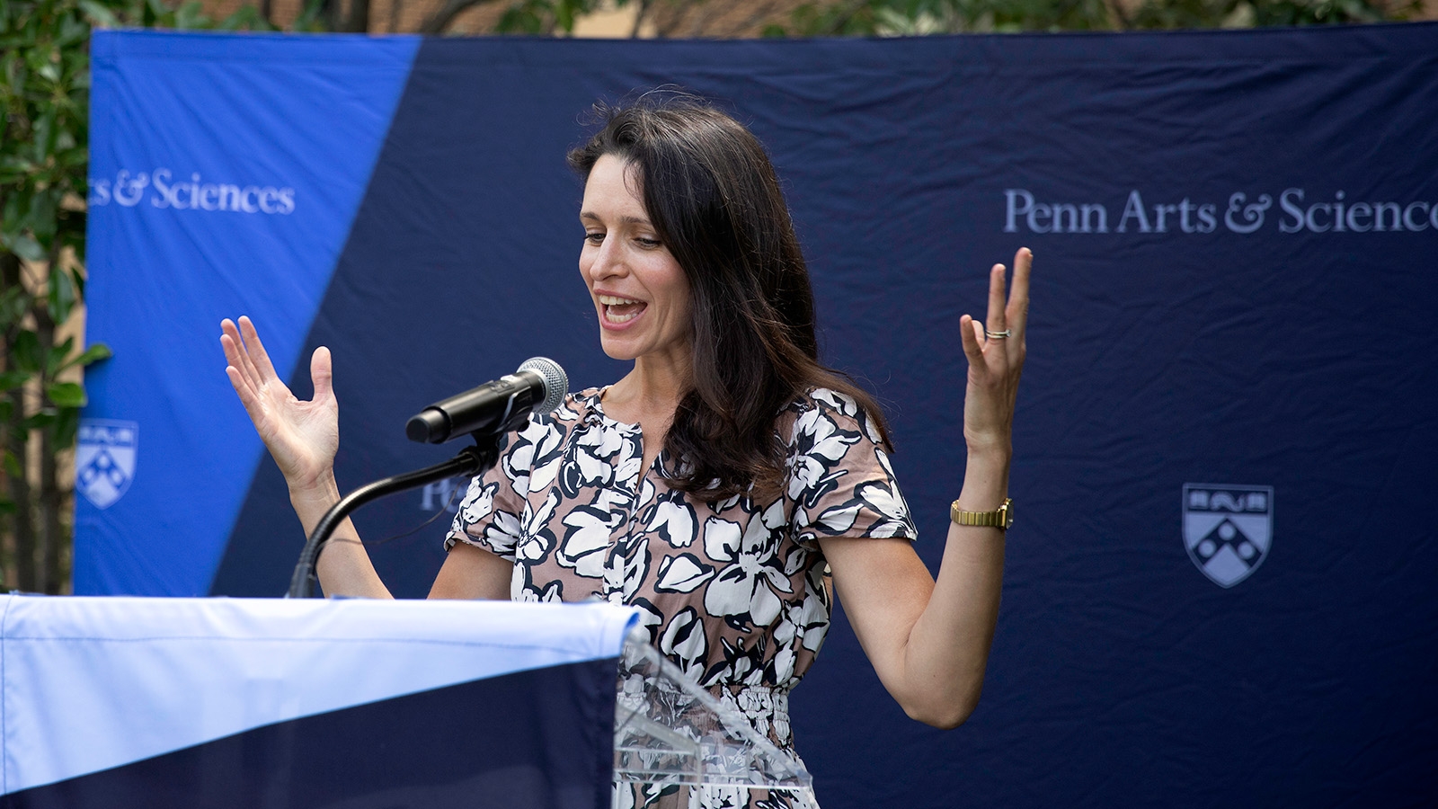 Mary Caldwell standing at a lecturn, with her arms up and outstretched. 